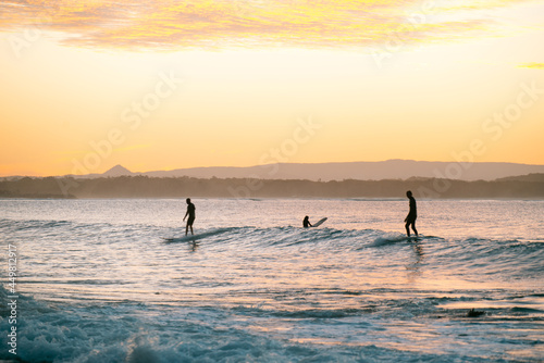 Fototapeta Naklejka Na Ścianę i Meble -  Silhouette of Surfers Riding a Wave at Sunset Time in Noosa,Queensland,Australia