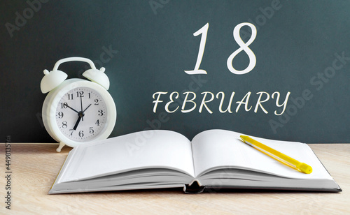 february 18. 18-th day of the month, calendar date.A white alarm clock, an open notebook with blank pages, and a yellow pencil lie on the table.Winter month, day of the year concept photo