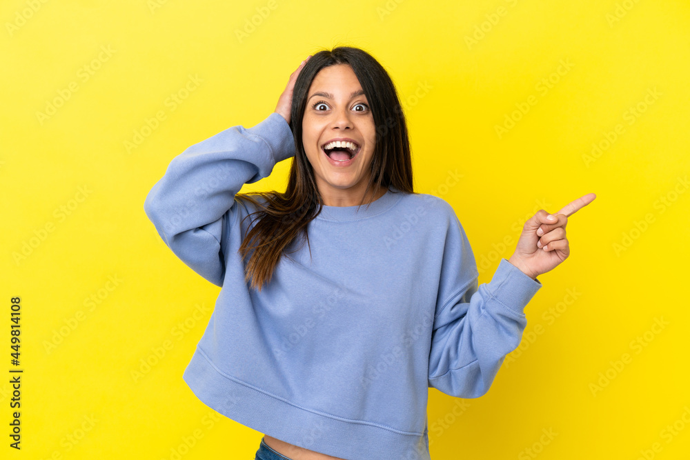 Young caucasian woman isolated on yellow background surprised and pointing finger to the side