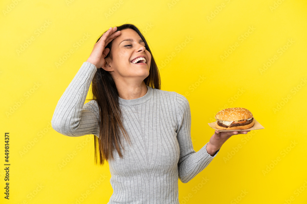 Young caucasian woman holding a burger isolated on yellow background smiling a lot Young caucasian woman holding a burger isolated on yellow background smiling a lot
