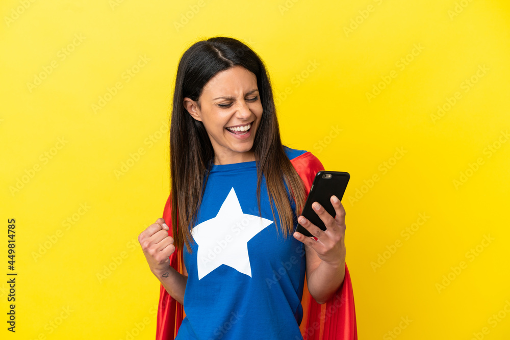 Super Hero woman isolated on yellow background using mobile phone and doing victory gesture Super Hero woman isolated on yellow background using mobile phone and doing victory gesture