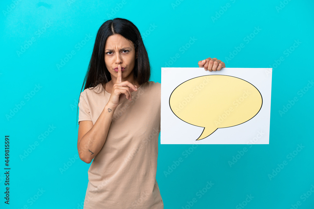 Young woman over isolated background holding a placard with speech bubble icon doing silence gesture Young woman over isolated background holding a placard with speech bubble icon doing silence gesture