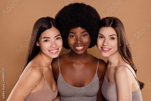 Photo of charming pretty three girlfriends wear crop tops smiling hugging isolated beige color background