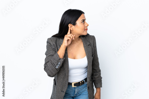 Young latin woman woman isolated on white background listening to something by putting hand on the ear