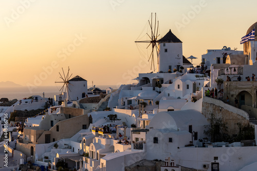 Whitewashed houses and windmills in Oia in warm rays of sunset on Santorini island. Greece