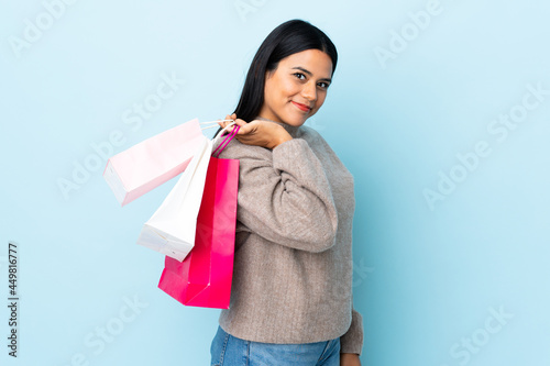 Young latin woman woman isolated on blue background holding shopping bags and smiling