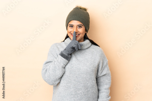 Young Colombian girl with winter hat isolated on beige background doing silence gesture © luismolinero