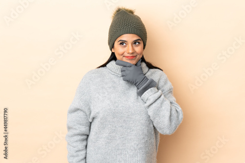 Young Colombian girl with winter hat isolated on beige background thinking an idea © luismolinero
