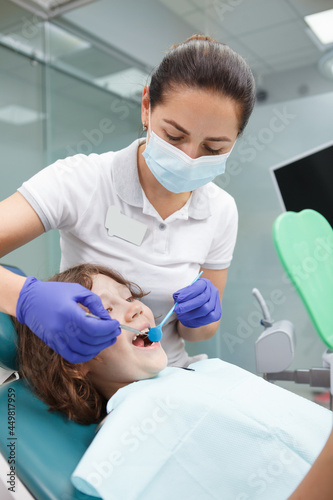 Vertical shot of a female dentist working at her clinic  treating teeth of young boy
