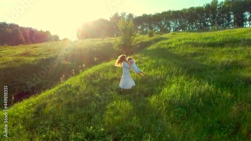 happy family is spinning in field. Mom and daughter turn, twist and laughing. Smile girl. drone flies away over hills. Aerial shot fly woman in white dress. run in green grass in summer sunny day. 