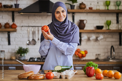 Cheerful Muslim woman showing a tomato and talking about ingredients