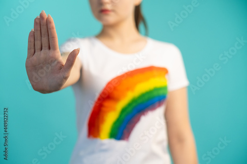 Stop homophobia. Gay discrimination. Equal rights. LGBT tolerance. Unrecognizable defocused woman with refusal hand gesture in t-shirt with colorful rainbow on blue background.