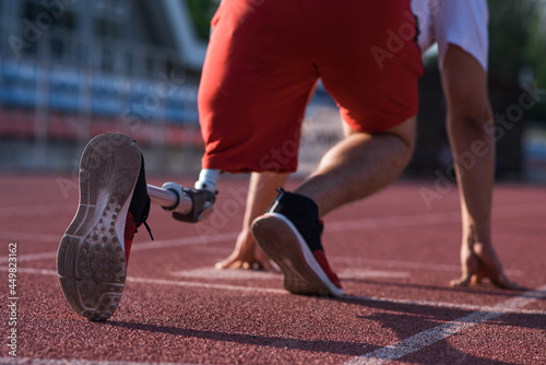 Caucasian male athlete with a prosthetic leg standing at the start on the track at the stadium. Back view. Sport concept.