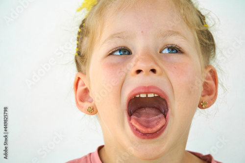 Cheerful child. Girl laughs close-up of the face on a white background. A little girl show tongue throat. portrait with wide open mouth and protruding tongue. with clear view pulls out long tongue