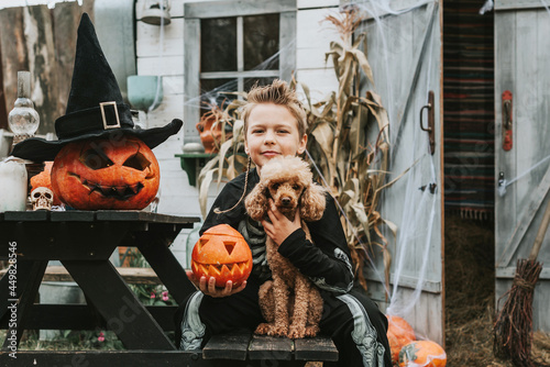 boy in a skeleton costume with a dog on the porch of a house decorated to celebrate a Halloween party