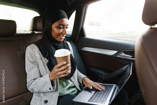 Black muslim woman working with laptop and drinking coffee in car