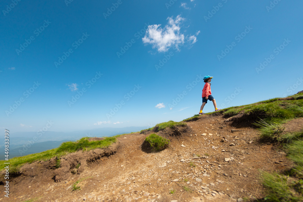 A child stands on the top of a mountain and looks into the distance