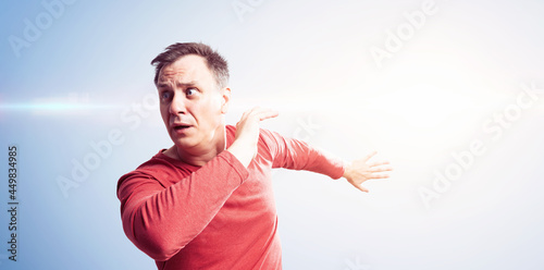 Emotionally scared man in red t-shirt running away from a bright flash from behind hiding behind his hands. Run away from danger concept.