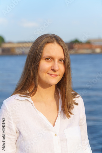 Portrait of beautiful young woman with long blonde hair standing on river embankment in city of St. Petersburg and looking to camera in sun shining, enjoing summer sunset. Copy space, vertical