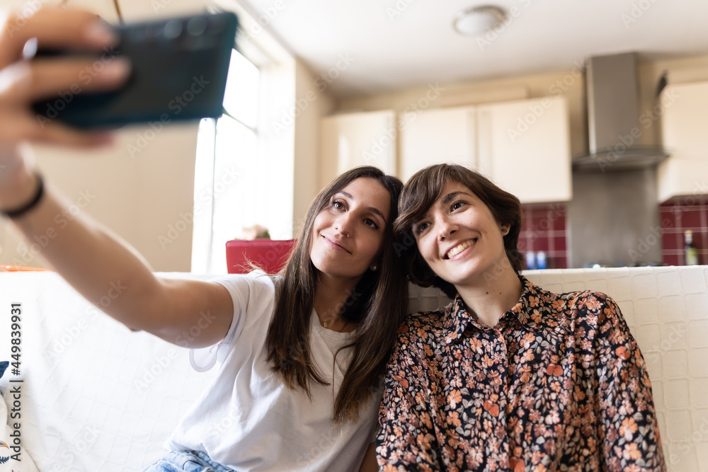 Photo of two attractive young females taking a selfie with their heads very close while sitting on a sofa at home Photo of two attractive young females taking a selfie with their heads very close while sitting on a sofa at home