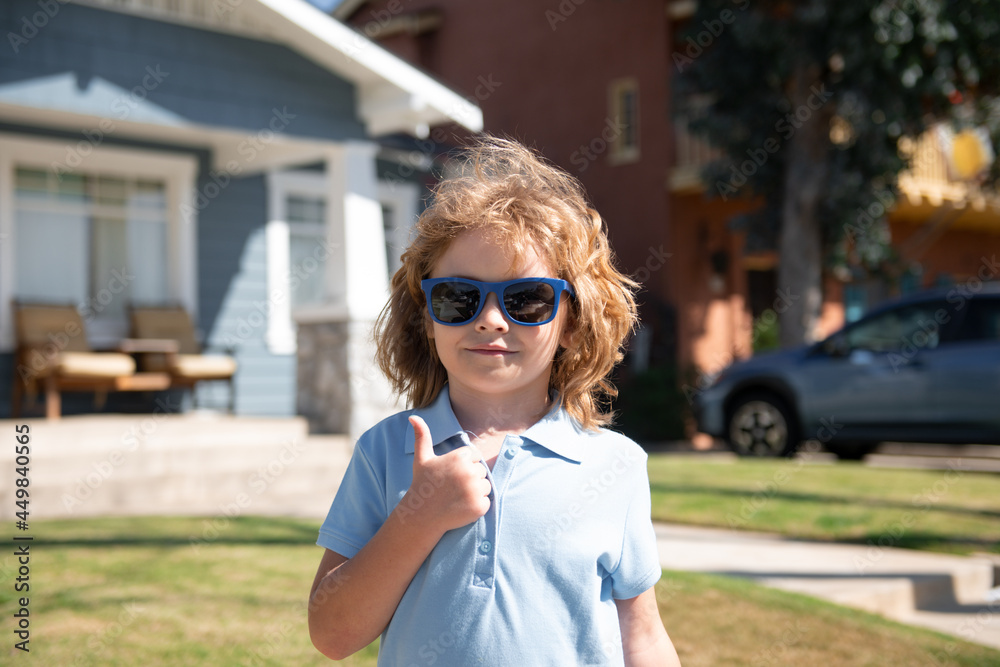 Funny child in sunglasses with thumbs up sign close up. Kids outdoor home, near house, head portrait. Funny child in sunglasses with thumbs up sign close up. Kids outdoor home, near house, head portrait.