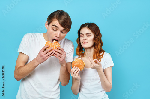 young couple in white t-shirts with hamburgers in their hands fast food snack