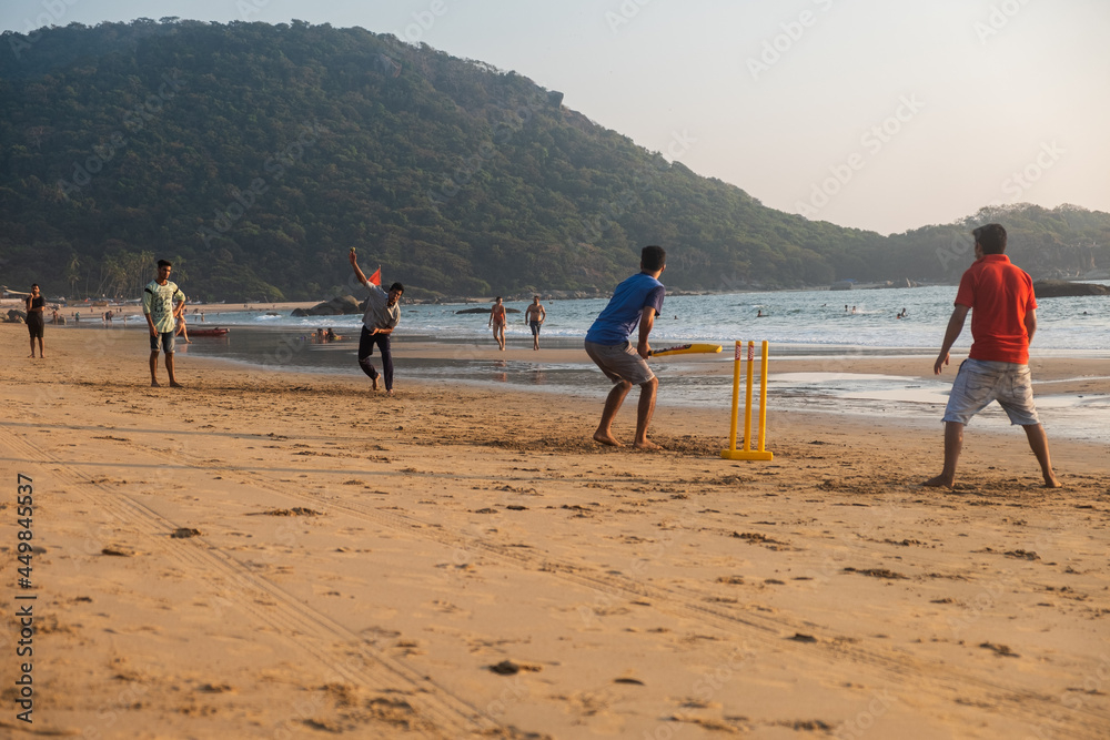 Group of Indian adults playing cricket on beach at sunset