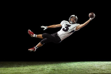 Portrait of American football player training isolated on dark studio background with green grass flooring. Concept of sport, competition