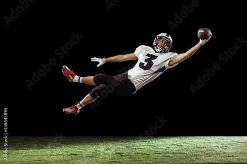 Принти на полотні Portrait of American football player training isolated on dark studio background with green grass flooring