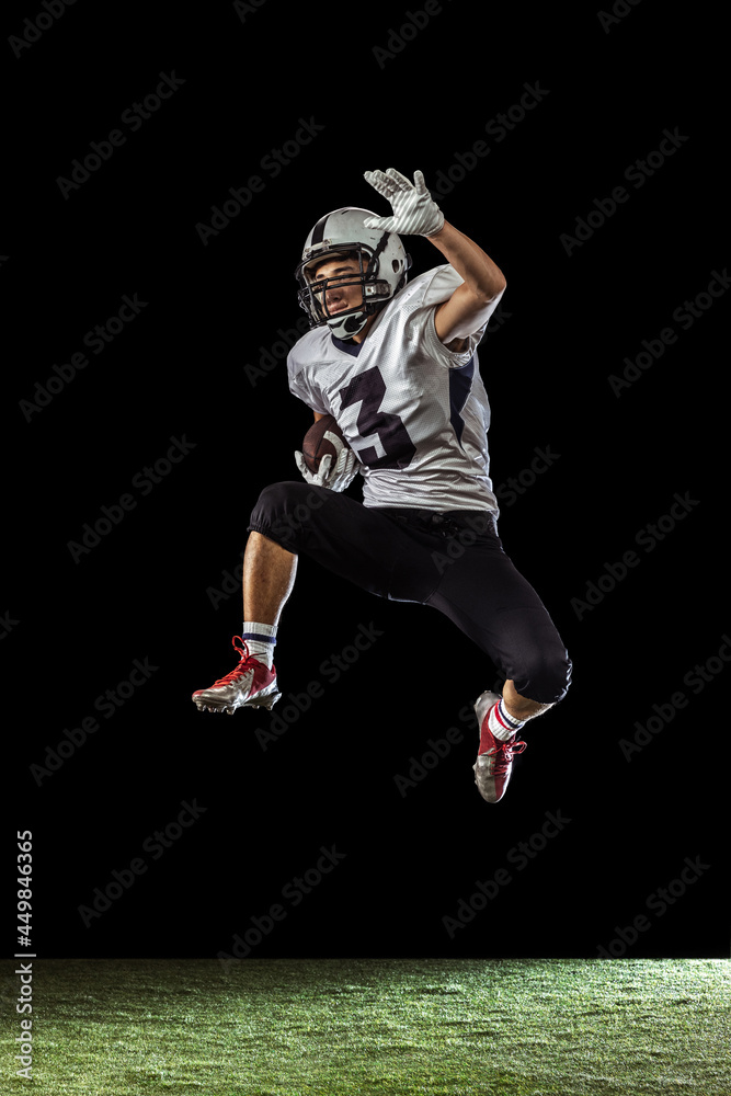 Portrait of American football player training isolated on dark studio background with grass flooring. Concept of sport, competition, goals, achievements