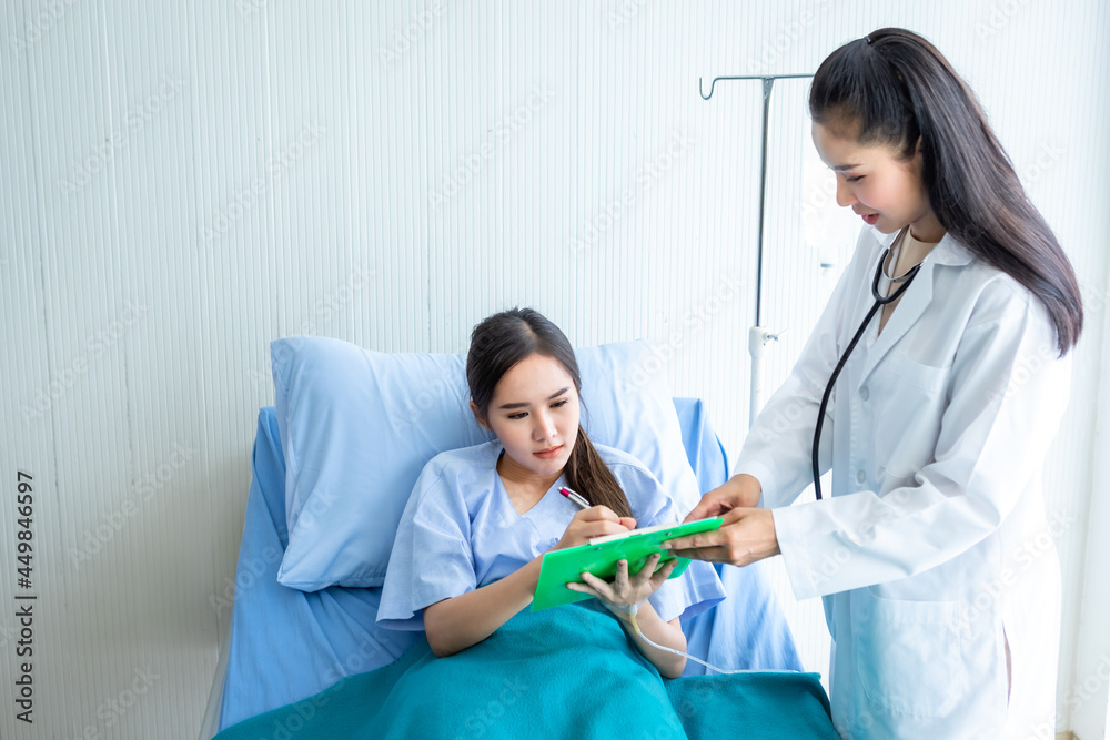 Asian young female patient Signature for consent form on bed to female doctor therapeutic advising with positive emotions in the room hospital background. Asian young female patient Signature for consent form on bed to female doctor therapeutic advising with positive emotions in the room hospital background.