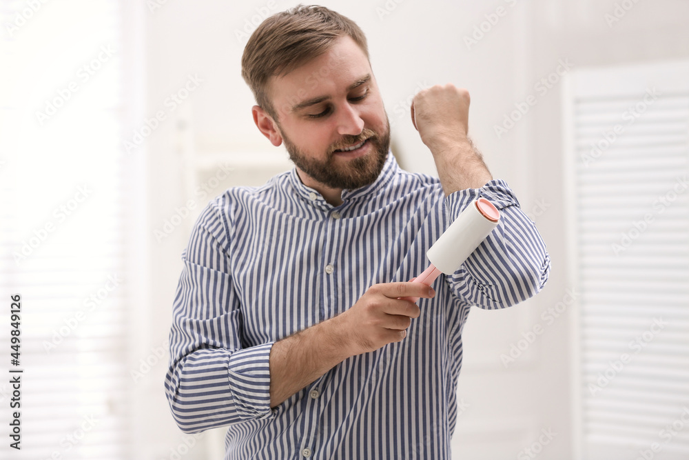 Young man cleaning clothes with lint roller at home Young man cleaning clothes with lint roller at home