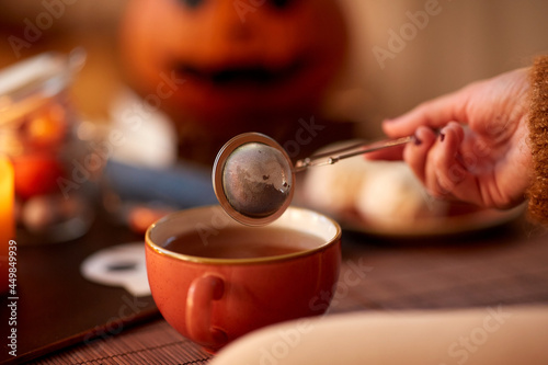 drinks, holidays and leisure concept - close up of woman's hand with mesh tea infuser ball and mug at home on halloween photo