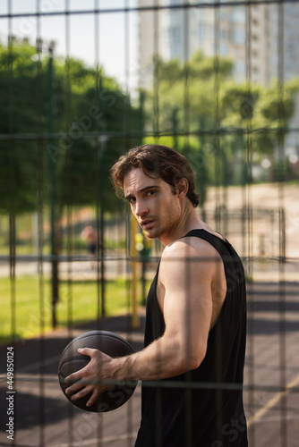 Young man with basketball ball looking at camera near fence outdoors © LIGHTFIELD STUDIOS