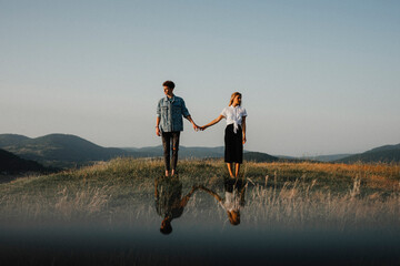 Young couple standing in nature in countryside, holding hands but looking away from each other.