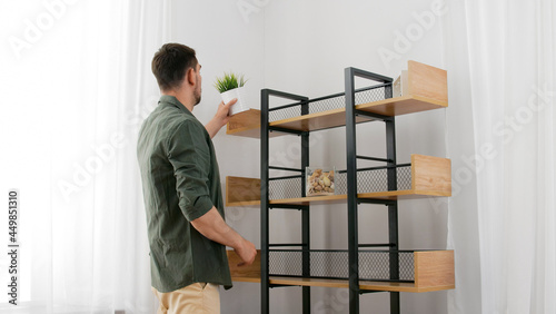 home improvement and decoration and people concept - man arranging shelf with flower in pot