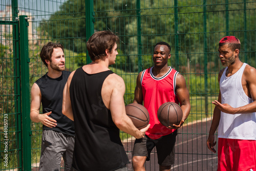 Cheerful african american man holding basketball ball near friends talking outdoors