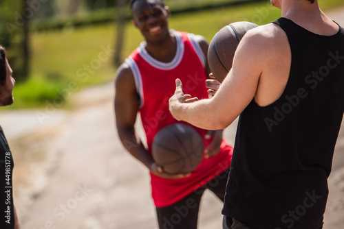 Sportsman holding basketball ball near blurred interracial friends outdoors