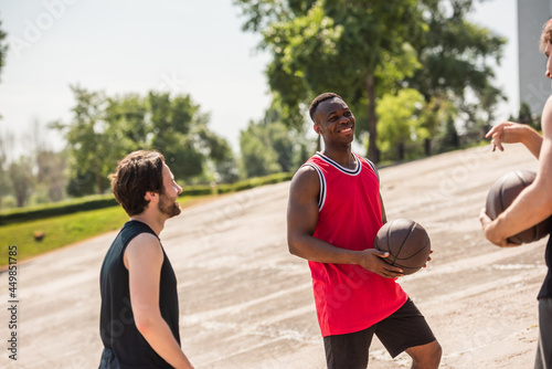 Cheerful african american basketball player with ball looking at friends outdoors © LIGHTFIELD STUDIOS