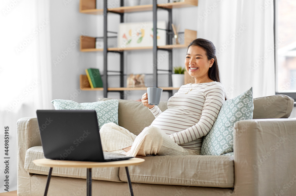 pregnancy, rest, people and expectation concept - happy smiling pregnant asian woman with laptop computer sitting on sofa at home and drinking tea pregnancy, rest, people and expectation concept - happy smiling pregnant asian woman with laptop computer sitting on sofa at home and drinking tea