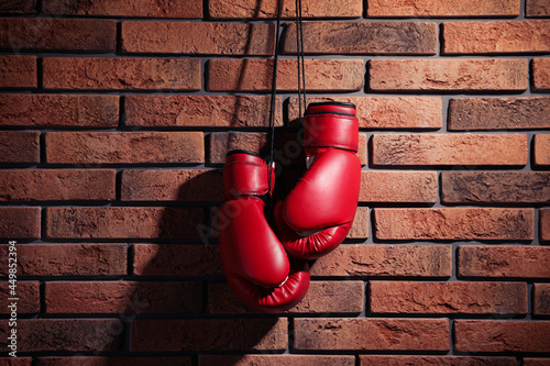 Pair of red boxing gloves hanging on brick wall