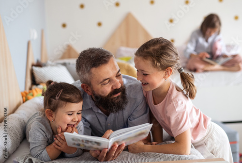 Father with three daughters indoors at home, reading a book. photo