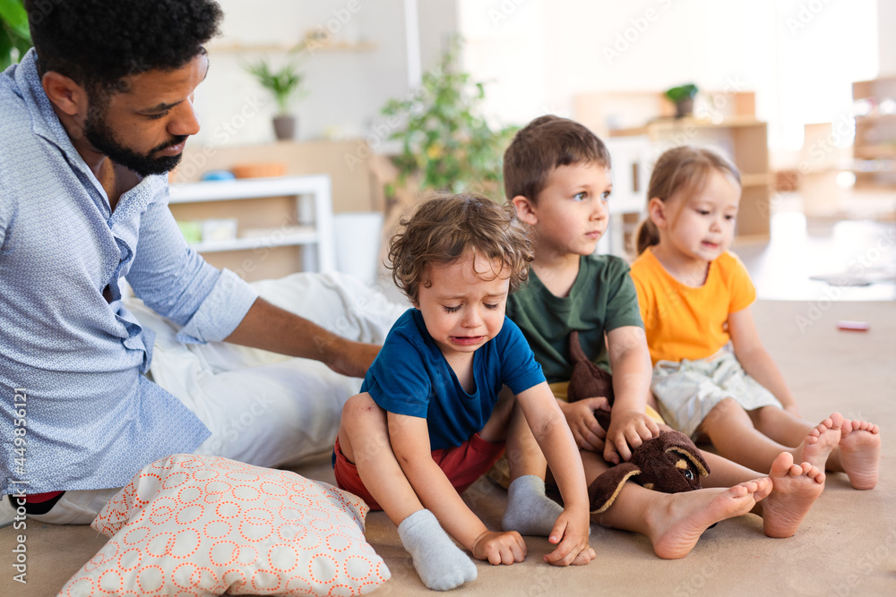 Man teacher comforting crying small boy in nursery school indoors in classroom. Man teacher comforting crying small boy in nursery school indoors in classroom.
