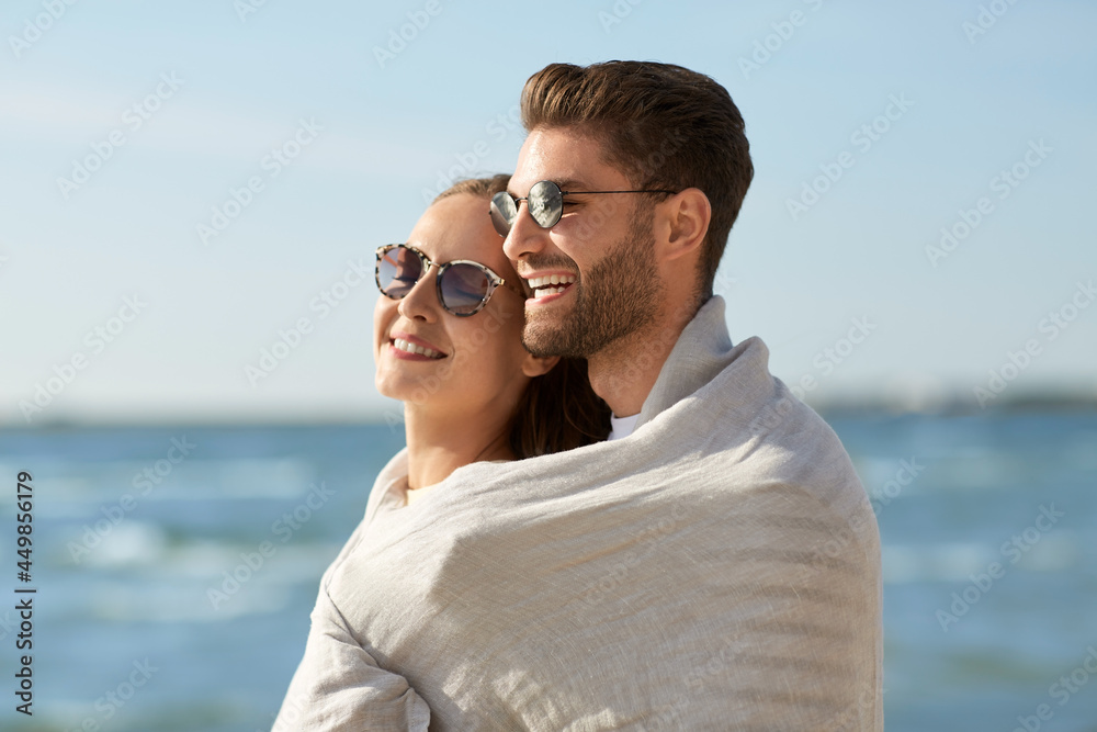 leisure, relationships and people concept - happy couple in sunglasses covered with blanket hugging on summer beach