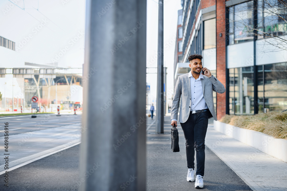 Portrait of young man student walking outdoors on street in city, using smartphone.