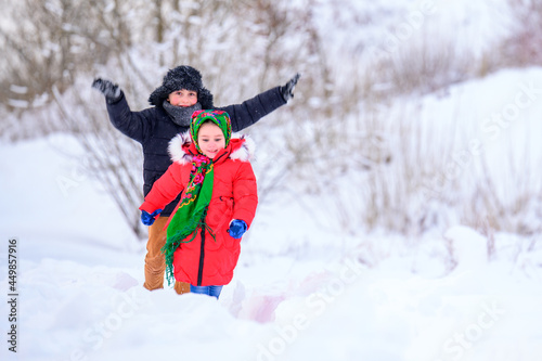 Brother and sister walk in a snowy yard, having fun with snow.