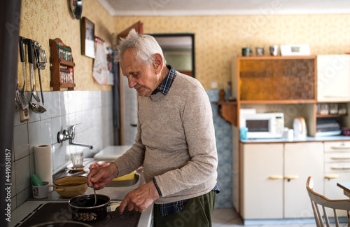 Portrait of elderly man cooking on stove indoors at home, stirring.