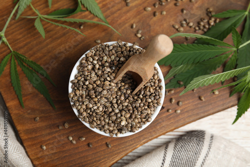 Organic hemp seeds and leaves on wooden board, flat lay