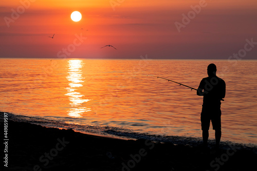 Sunrise above the black sea with the silhouette of a fisherman on the beach.
