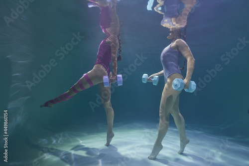 two girls go in for sports in the pool underwater on a blue background